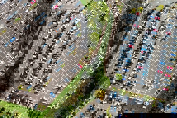 Aerial view of several busy car parks beside intersecting roads, showing rows of parked vehicles, marked bays, access routes and surrounding green spaces.